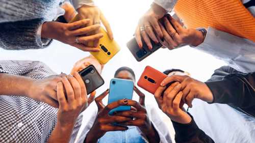 A photograph looking up at a group of five people looking down towards mobile phones in their hands